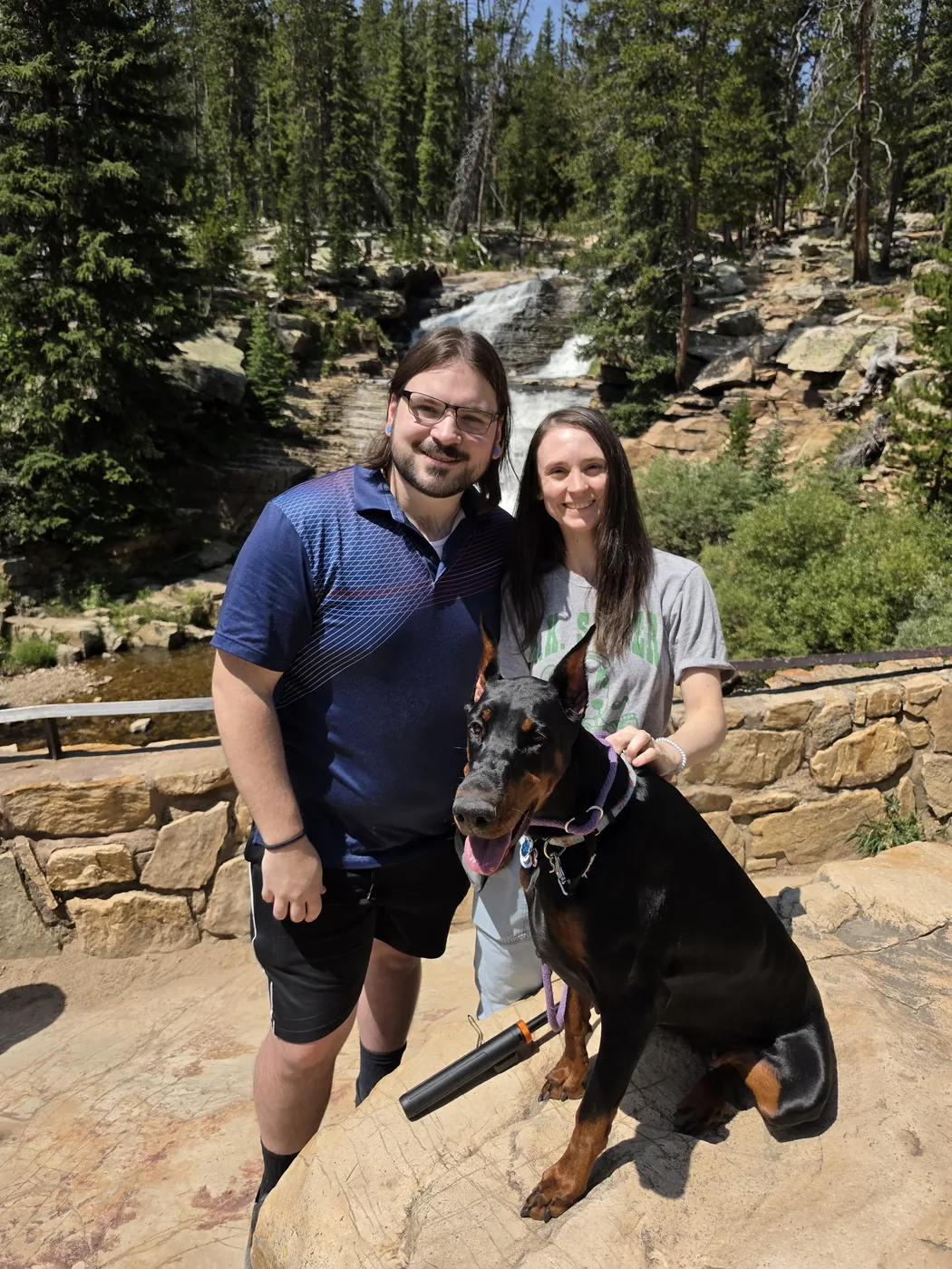 Evanelle sitting between her two people on a rock overlook in front of a mountain waterfall